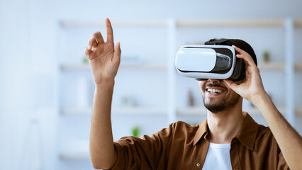 A man with a joyful expression is fully engaged in a virtual reality experience. He is wearing a VR headset and actively using his hands to interact.