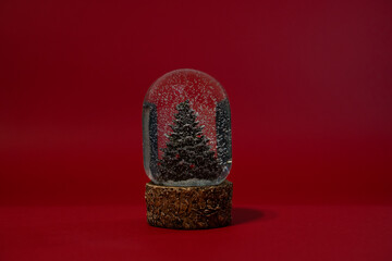 A glass snow globe featuring a miniature Christmas tree inside, with delicate white snowflakes gently falling around it. Festive holiday decoration set in a serene winter atmosphere.