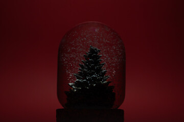 A glass snow globe featuring a miniature Christmas tree inside, with delicate white snowflakes gently falling around it. Festive holiday decoration set in a serene winter atmosphere.