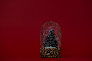 A glass snow globe featuring a miniature Christmas tree inside, with delicate white snowflakes gently falling around it. Festive holiday decoration set in a serene winter atmosphere.