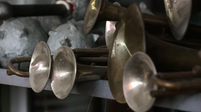 A close-up view of numerous brass instrument bells, possibly trumpets or cornets, stacked together. The aged metal reflects light, showcasing musical history and craftsmanship.