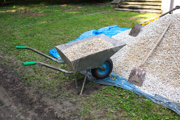 Wheelbarrow in the garden - garden work. Wheelbarrow filled with gravel. Filling a wheelbarrow with...