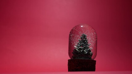 A glass snow globe featuring a miniature Christmas tree inside, with delicate white snowflakes gently falling around it. Festive holiday decoration set in a serene winter atmosphere. 4 k video - Powered by Adobe