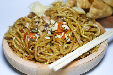 A bowl of spicy fried noodles with wonton crackers in a bowl, isolated on a white background with a wooden plate and traditional chopsticks