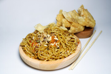 A bowl of spicy fried noodles with wonton crackers in a bowl, isolated on a white background with a wooden plate and traditional chopsticks