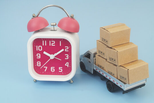 Lorry truck with cardboard boxes and alarm clock on blue background. Shipping and delivery time concept.