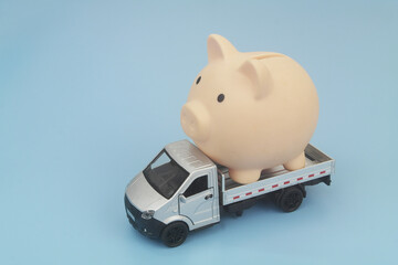 Lorry truck with piggy bank on blue background. Shipping and delivery cost, financial fund relocation and moving money concept. © Valerii Evlakhov