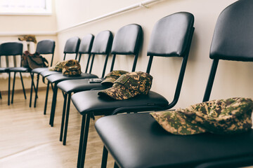 Row of empty chairs with military camouflage caps placed neatly on seats