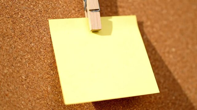 Blank yellow sticky note pinned to a cork board with a wooden clothespin