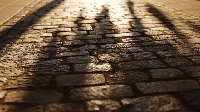Sunlit cobblestone street with dramatic shadows, textured urban pathway footage