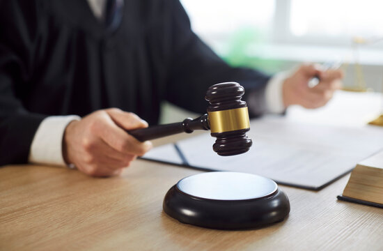 Man judge knocking gavel wearing robe having court verdict sitting at the desk on workplace in courtroom. Closeup of male justice worker working indoors. Legal law and justice concept.