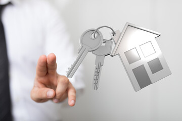 Hand pointing to house keys and a house-shaped keyring, symbolizing home ownership, real estate, and the concept of buying a property. Ideal for