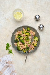 Fried broccoli with bacon and canned white beans on a gray plate against a light concrete background. Broccoli recipes.