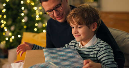 A young boy enjoys the gift from Santa Claus, tears the colored paper, and finds a large box with a...