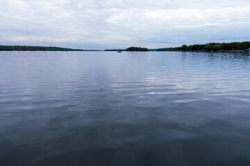 A wide view of Pewaukee Lake in Waukesha County, Wisconsin, featuring smooth blue water, a distant boat, and a shoreline under cloudy October skies.