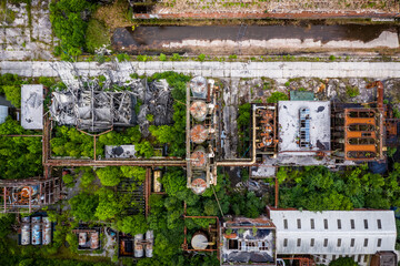 Aerial view of overgrown abandoned industrial complex with rusted tanks and pipelines