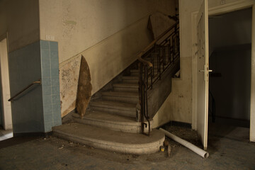 Derelict staircase in an abandoned hospital corridor with peeling paint and blue tiles