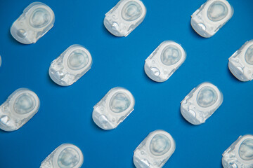 Coloring diagonally: one-day contact lenses lie diagonally in a disposable protective case, in which transparent lenses float, which lie on a blue background at the same distance. The concept of