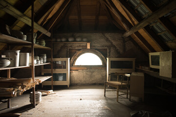 Sunlit abandoned attic in derelict spa hotel with wooden beams, shelves of vintage ceramics and an antique chair