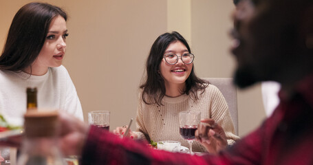 A guy with a beard, a multi-ethnic boy, listens as a girl of Asian descent in glasses explains the method of preparation for a dish at the table. The brunette sits and tells him about the food.