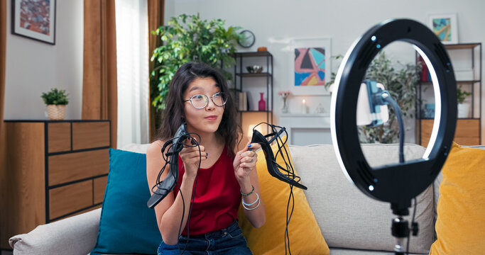 Confident fashion vlogger relaxes on a sofa and displays her latest shoe find, presenting trendy high heel footwear to viewers in a professionally shot video for social media.