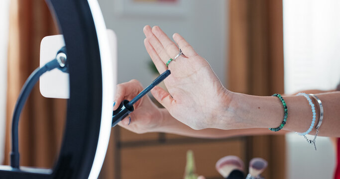 Beauty Blogging. Girl doing eyelash make up recording beauty product review showing mascara brush on hand. Makeup artist shooting video for her channel using cell phone on tripod.