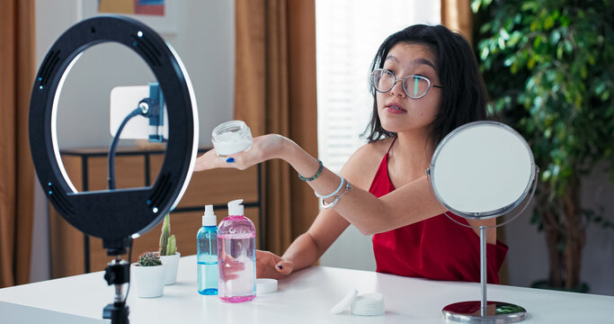 Beauty influencer shares skincare tips while applying moisturizer to her face. She records the video blog with her smartphone, explaining beauty treatments step by step.