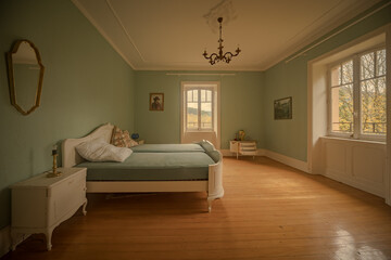 Empty vintage bedroom in an abandoned chateau with chandelier, large windows and warm natural light