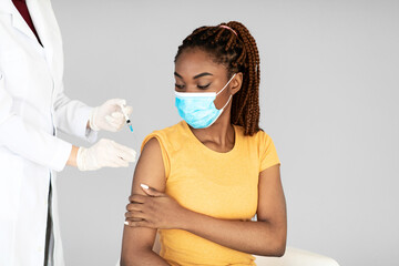 A medical doctor gives a covid-19 vaccine shot to a young black woman wearing a face mask. This scene highlights participation in a vital immunization campaign.