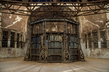 Rusting circular machinery inside an abandoned wastewater treatment plant with peeling plaster, tiled walls and broken windows