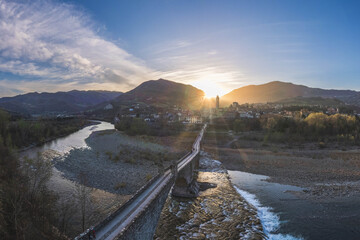 Aerial view of the medieval stone bridge crossing the Trebbia River at sunset with the town and hills in the background, Bobbio, Emilia-Romagna, Italy