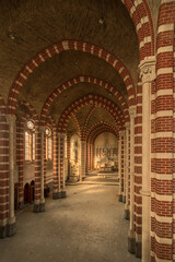 Sunlit empty nave of an abandoned red-brick monastery church with striped arches, vaulted ceiling and ornate altar