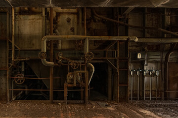 Rusted pipes and valve wheels inside a dark, derelict paper mill - atmospheric industrial interior