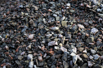 Gravel of various colors is stacked on a construction site, prepared for use in landscaping and building projects under clear skies