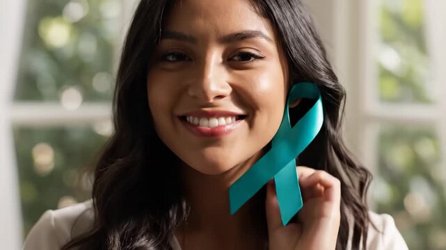 Woman Holding Teal Awareness Ribbon - A young woman with dark hair is holding a teal ribbon up to her ear, smiling gently with her eyes closed.