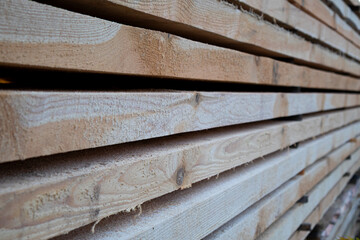 Rows of smooth wooden planks are neatly stacked in a lumberyard, showing their natural texture and grain under bright sunlight
