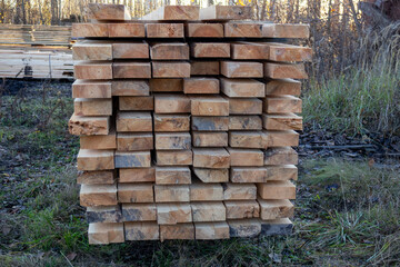 Freshly cut wooden planks are neatly stacked outdoors, drying in the sun at a timber yard surrounded by autumn foliage