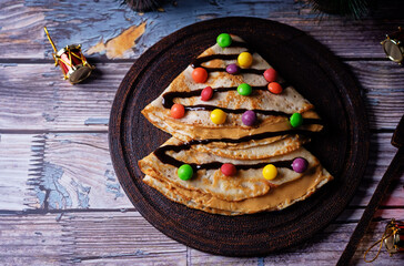 Fried crepes with peanut butter filling and chocolate and multicolored candies topping in the form of Christmas tree