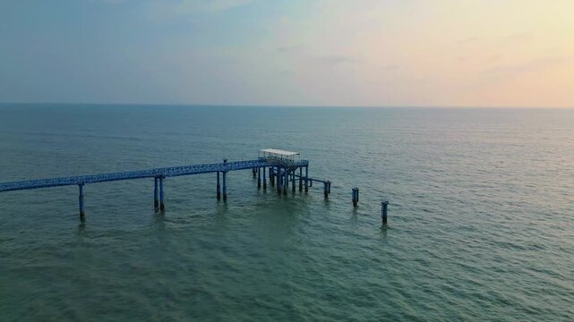 A serene drone shot of Jetty Ghat in Coxs Bazar during sunset, capturing calm waves, golden light, and the peaceful seaside atmosphere of the world&rsquo;s longest natural sea beach.