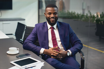 Handsome african american young businessman in nice suit sitting at table with documents, smartphone, digital tablet, drinking coffee at conference hall in office, having business meeting, copy space
