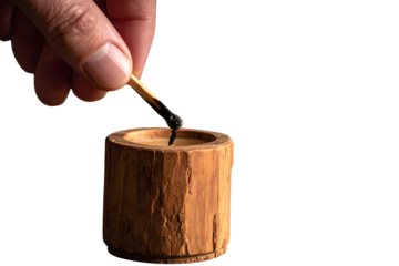 A person's hand holding an extinguished match over a rustic wooden candle holder, isolated on a white background