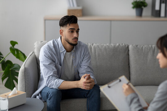 Young Arab man appears distressed while discussing his depression with a counselor in a clinic office. The setting is calm and supportive, focusing on mental health treatment.