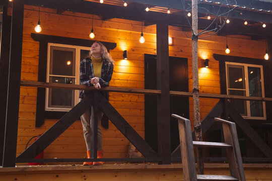 Woman in an oversized cozy sweater and boots enjoys the golden hour on a rustic porch, surrounded by nature. Peaceful and serene outdoor moment embracing simplicity