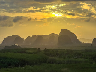 A dramatic golden sunrise unfolds above the silhouetted limestone karsts, casting a warm, ethereal...