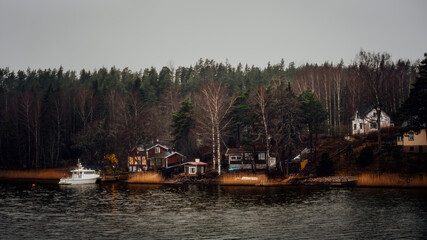 Scandinavian lakeside scenery with small wooden houses, forest and a boat near the shore on a calm...