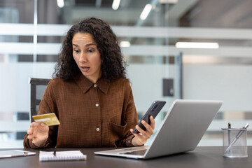 Woman reacting with shock and concern while holding a credit card and smartphone, finding an issue with her online purchase or realizing a security breach