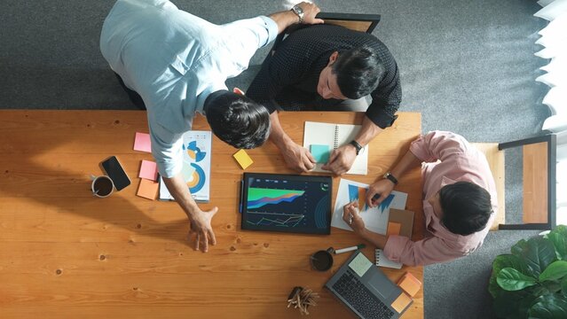 Top view of skilled project manager talking about financial graph to investors while sitting at meeting table with data analysis document. Diverse team discussing and brainstorming idea. Convocation.