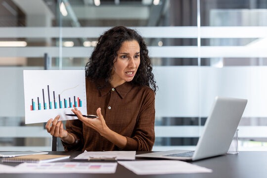 Frustrated businesswoman showing a declining bar chart on her laptop during a virtual meeting, delivering bad financial news with upset, stressed expression in modern office - Powered by Adobe