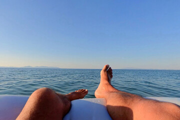 man feet sitting on inflatable boat over the sea. Holiday concept. man feet relaxing on beach, enjoying sun and splendid view. barefoot sunbathing on summer beach. Happy on holidays vacation concept.
