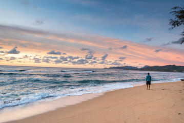 Tourist walking alone on sandy beach at sunset, enjoying beautiful ocean view in kauai, hawaii